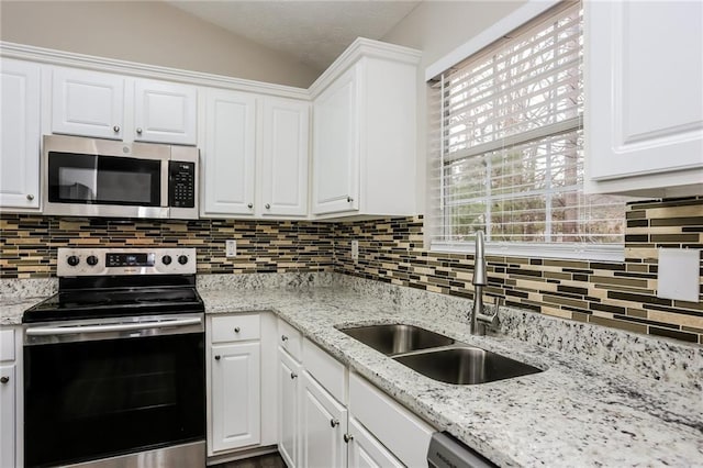 kitchen featuring a sink, white cabinetry, appliances with stainless steel finishes, vaulted ceiling, and tasteful backsplash