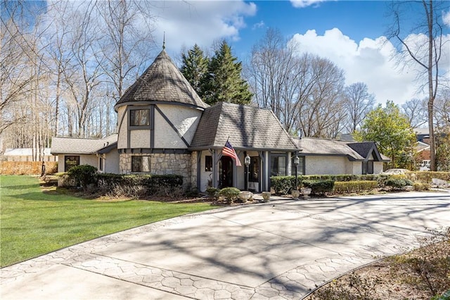 tudor house featuring stone siding, concrete driveway, a front lawn, and stucco siding