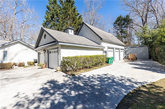 view of side of home with an attached garage, a shingled roof, concrete driveway, and stucco siding