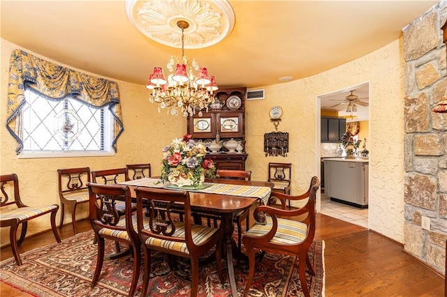 dining space featuring ceiling fan with notable chandelier, visible vents, a textured wall, and wood finished floors