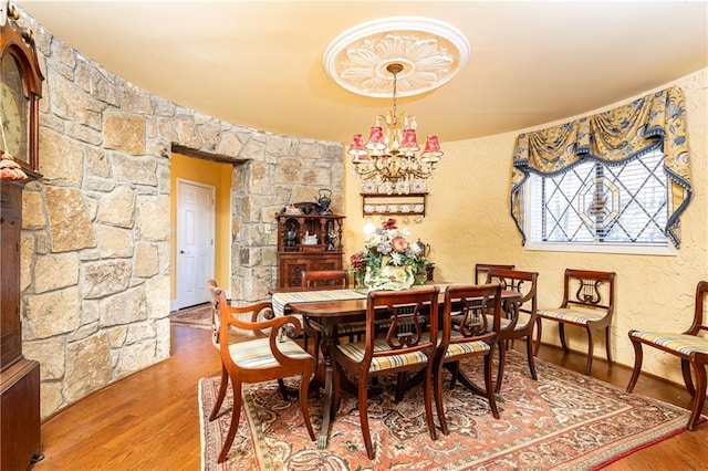 dining space featuring a notable chandelier, wood finished floors, and a textured wall