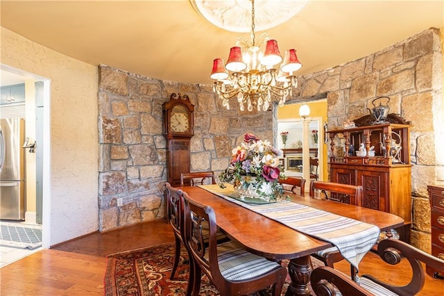 dining space featuring a chandelier, a textured wall, wood finished floors, and decorative columns