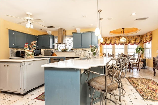 kitchen featuring a breakfast bar, a peninsula, island exhaust hood, a tray ceiling, and light countertops