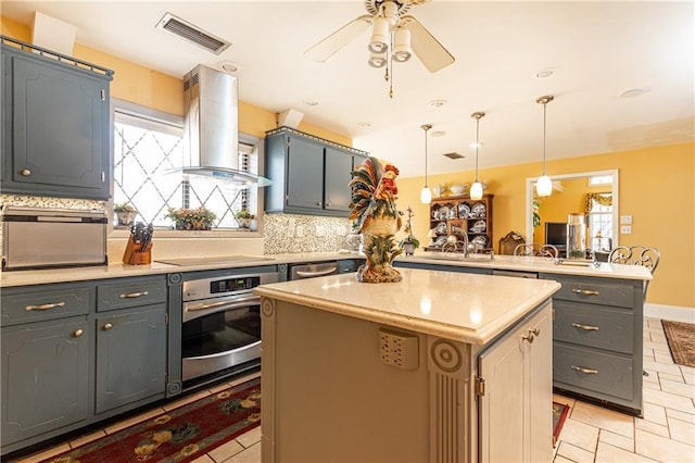 kitchen with island range hood, a peninsula, visible vents, appliances with stainless steel finishes, and tasteful backsplash