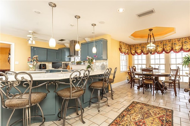 kitchen with tasteful backsplash, visible vents, a raised ceiling, light countertops, and wall chimney range hood