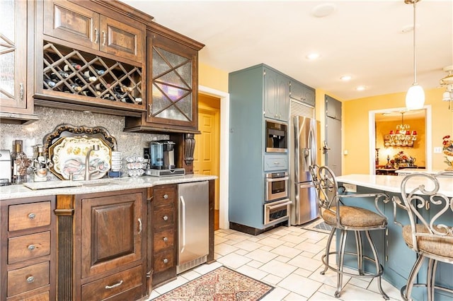 kitchen with a sink, hanging light fixtures, appliances with stainless steel finishes, tasteful backsplash, and a kitchen bar