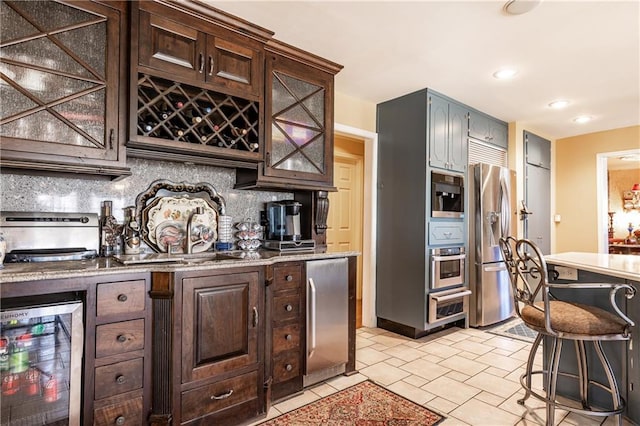 kitchen featuring beverage cooler, a sink, dark brown cabinets, appliances with stainless steel finishes, and tasteful backsplash