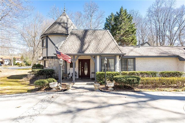 tudor-style house with stone siding, roof with shingles, and stucco siding