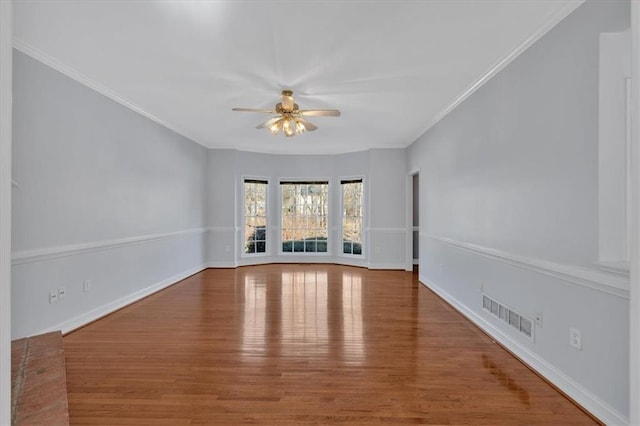 empty room featuring a ceiling fan, baseboards, wood finished floors, visible vents, and ornamental molding