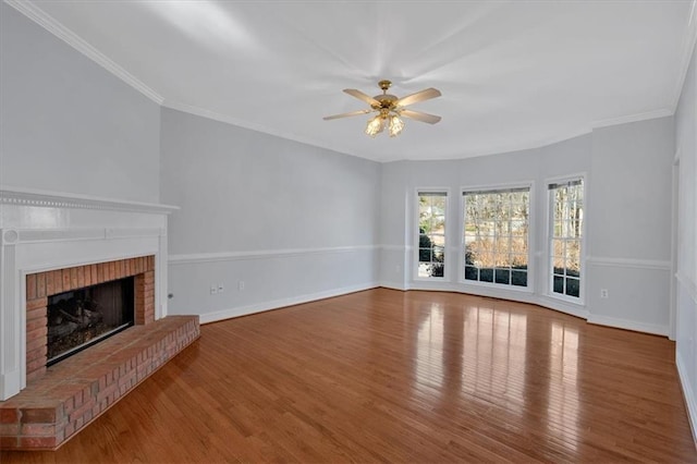 unfurnished living room with ornamental molding, a brick fireplace, baseboards, and wood finished floors