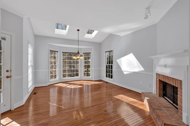 unfurnished living room featuring baseboards, an inviting chandelier, wood-type flooring, lofted ceiling with skylight, and a brick fireplace