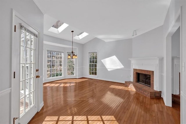 unfurnished living room featuring baseboards, vaulted ceiling with skylight, a fireplace, hardwood / wood-style flooring, and a notable chandelier