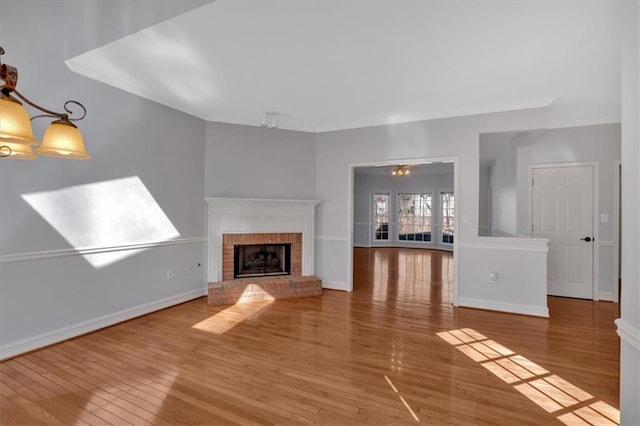 unfurnished living room with baseboards, a brick fireplace, wood finished floors, and crown molding