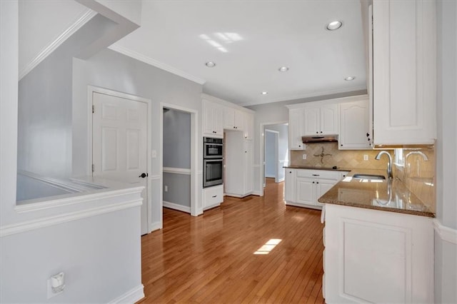 kitchen featuring light wood finished floors, a sink, white cabinets, under cabinet range hood, and tasteful backsplash