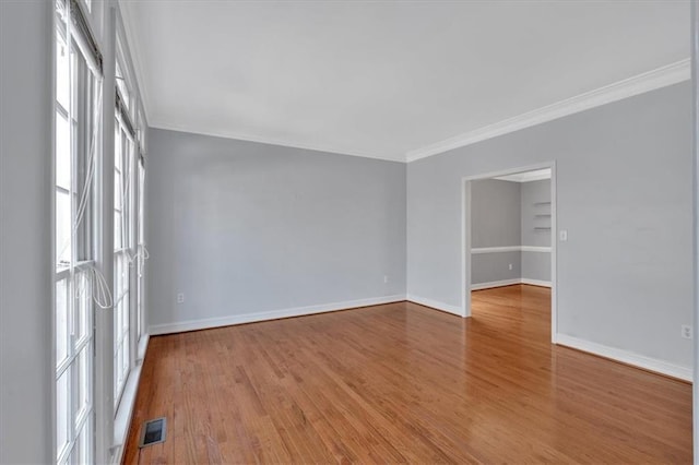 empty room with crown molding, wood finished floors, visible vents, and baseboards