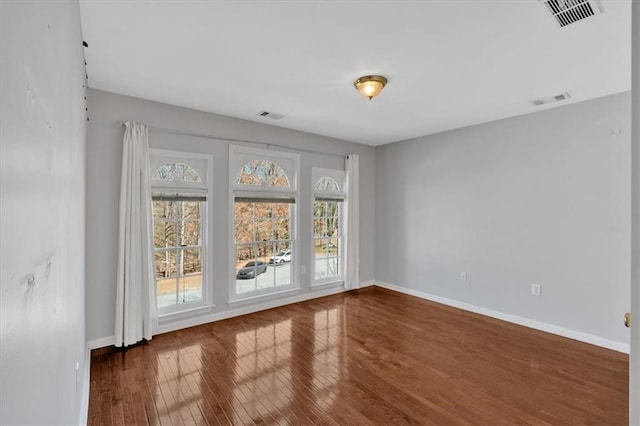 unfurnished room with visible vents, baseboards, and hardwood / wood-style flooring