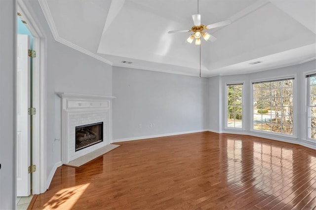 unfurnished living room featuring a tray ceiling, visible vents, a fireplace with flush hearth, and wood finished floors