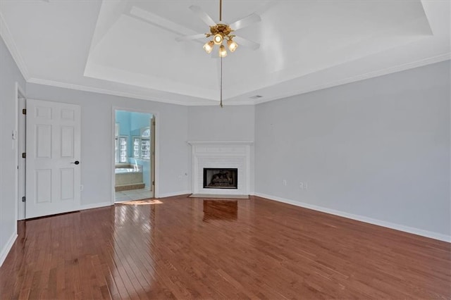 unfurnished living room with a tray ceiling, a fireplace with flush hearth, wood finished floors, and baseboards