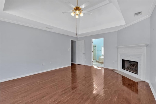 unfurnished living room featuring a fireplace with flush hearth, a ceiling fan, a tray ceiling, and wood finished floors