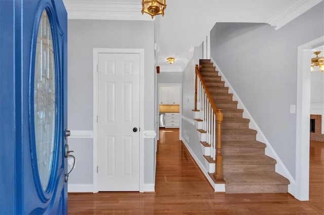 entryway with stairway, wood finished floors, baseboards, and ornamental molding