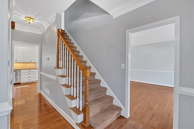 stairs featuring wood finished floors, baseboards, and ornamental molding