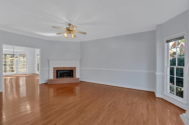 unfurnished living room featuring wood finished floors, baseboards, a fireplace, crown molding, and ceiling fan with notable chandelier