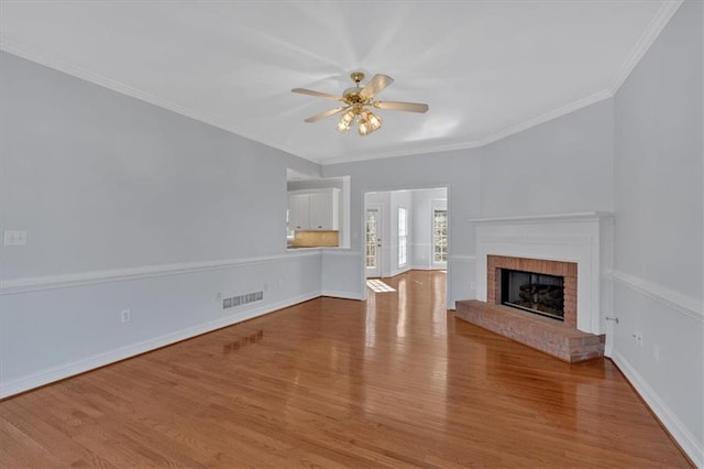 unfurnished living room featuring baseboards, wood finished floors, visible vents, and ornamental molding