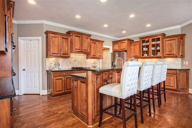 kitchen featuring stainless steel fridge with ice dispenser, dark hardwood / wood-style floors, dark stone counters, a kitchen island with sink, and a breakfast bar