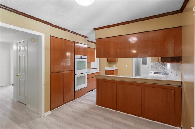 342 Spring Valley Rd, Waynesboro, GA 30830 - kitchen featuring brown cabinetry, white double oven, a sink, crown molding, and light wood finished floors
