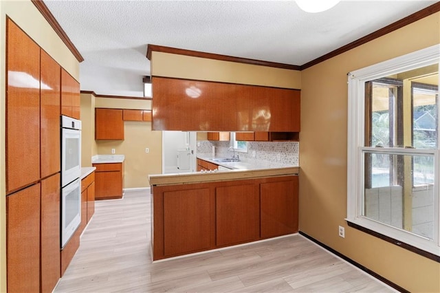 342 Spring Valley Rd, Waynesboro, GA 30830 - kitchen featuring brown cabinets, crown molding, a peninsula, decorative backsplash, and light countertops