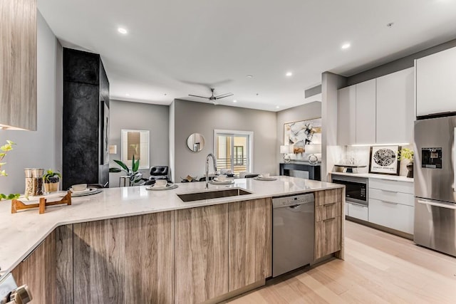 kitchen featuring stainless steel appliances, ceiling fan, sink, white cabinetry, and light hardwood / wood-style floors