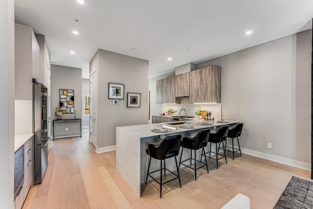 kitchen with light wood-type flooring, light stone counters, kitchen peninsula, and a breakfast bar