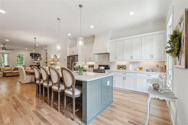 kitchen with appliances with stainless steel finishes, light countertops, premium range hood, white cabinetry, and pendant lighting