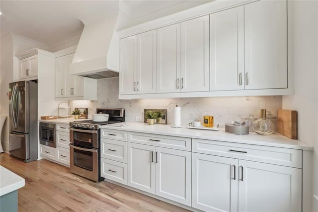 kitchen with premium range hood, white cabinetry, light wood-style floors, light countertops, and appliances with stainless steel finishes