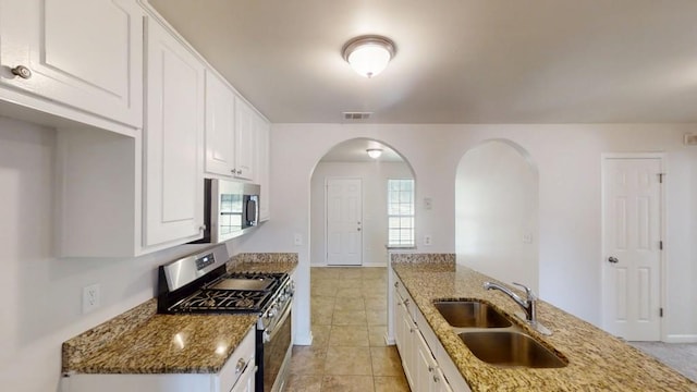 kitchen with appliances with stainless steel finishes, a sink, arched walkways, and light stone countertops