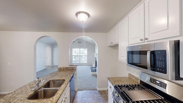 kitchen with stainless steel appliances, a sink, arched walkways, light stone counters, and light colored carpet