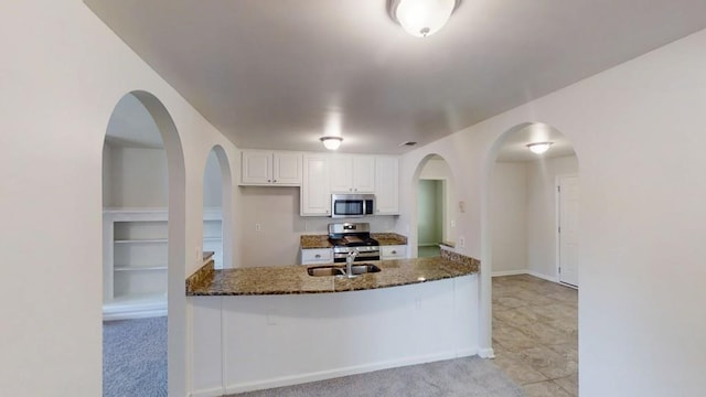 kitchen featuring appliances with stainless steel finishes, dark stone countertops, a sink, white cabinets, and a peninsula