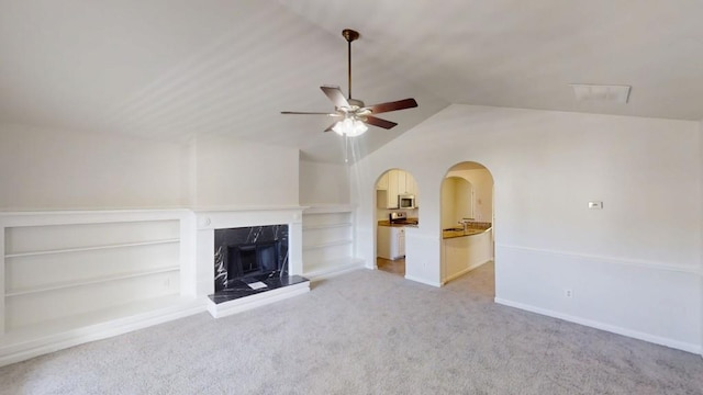 unfurnished living room featuring a high end fireplace, light colored carpet, ceiling fan, baseboards, and vaulted ceiling