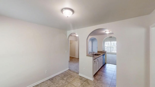 kitchen featuring arched walkways, a sink, baseboards, light tile patterned floors, and white cabinetry