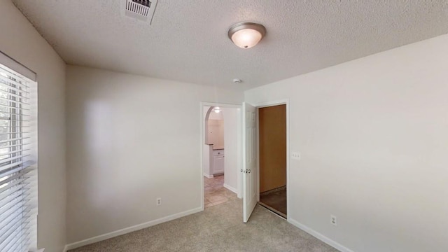 empty room featuring arched walkways, light colored carpet, a textured ceiling, and baseboards