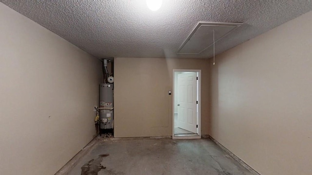 empty room featuring attic access, gas water heater, unfinished concrete floors, and a textured ceiling