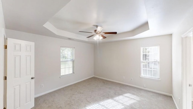 spare room featuring a raised ceiling, ceiling fan, light colored carpet, and healthy amount of natural light