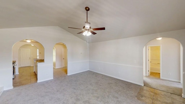 spare room with ceiling fan, arched walkways, light colored carpet, vaulted ceiling, and baseboards