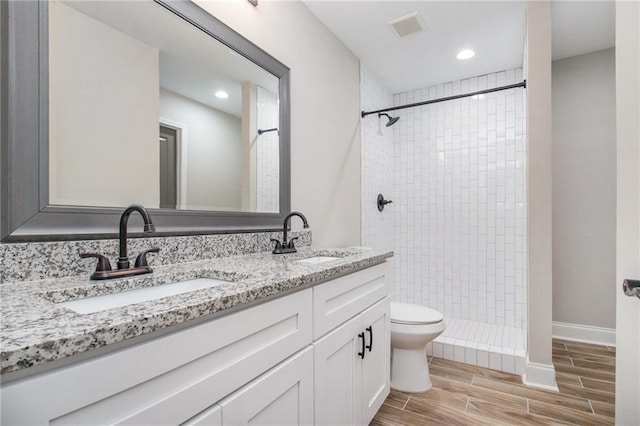 bathroom featuring a tile shower, vanity, and toilet