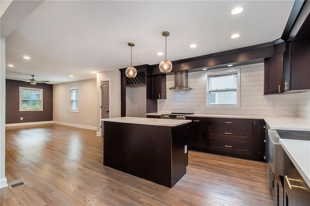 kitchen featuring tasteful backsplash, a center island, light hardwood / wood-style flooring, hanging light fixtures, and wall chimney range hood