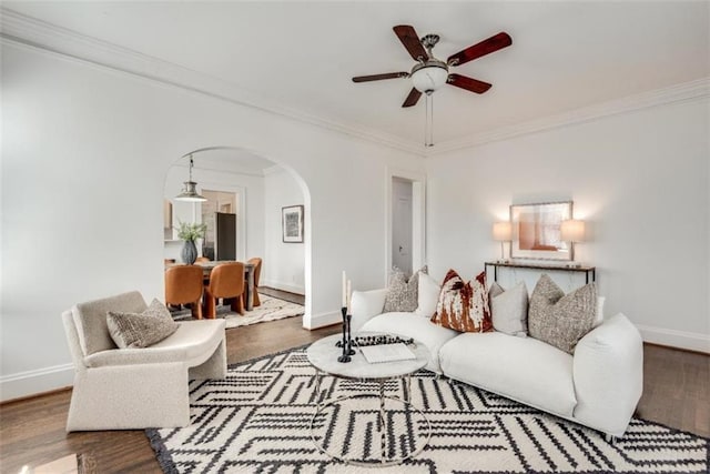 living area featuring arched walkways, ceiling fan, wood finished floors, baseboards, and crown molding