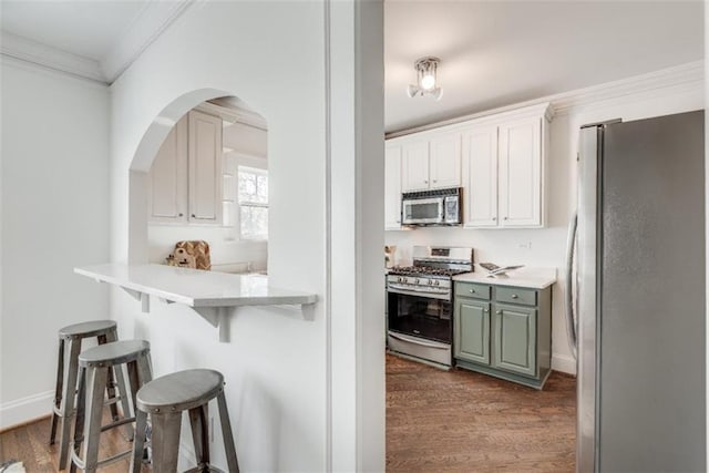 kitchen with dark wood finished floors, a breakfast bar area, stainless steel appliances, light countertops, and ornamental molding