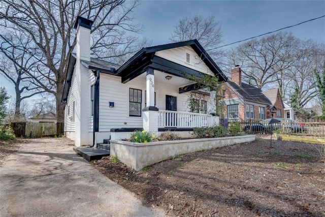 view of front of home featuring covered porch, fence, and a chimney