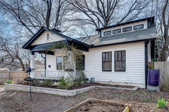 bungalow featuring a porch, a shingled roof, fence, and a garden