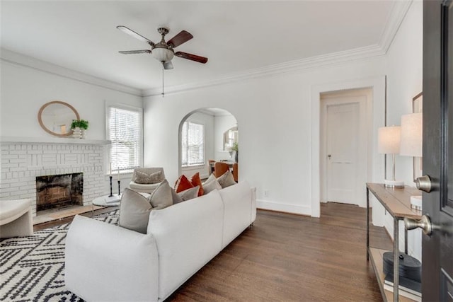 living area featuring arched walkways, a ceiling fan, ornamental molding, wood finished floors, and a brick fireplace